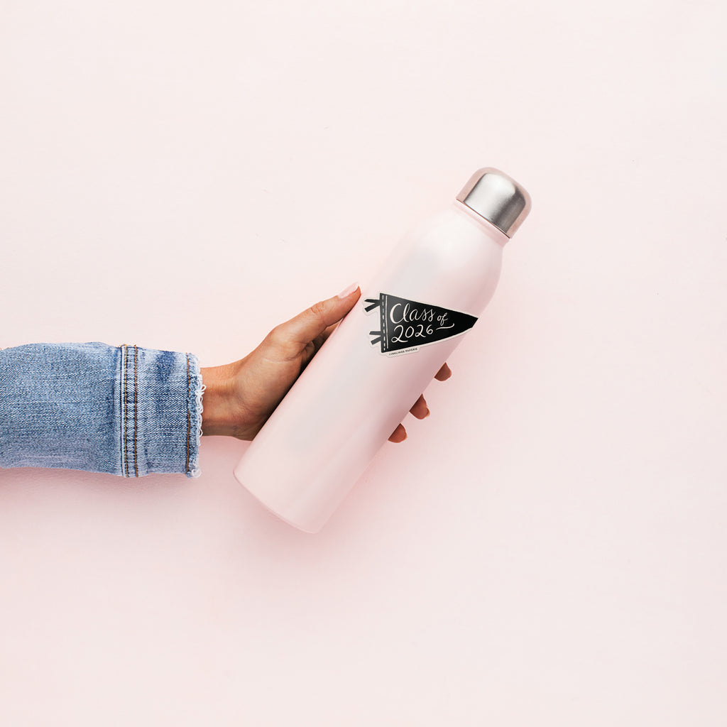 Hand holding a pink water bottle with a 'Class of 2026' vinyl sticker in a black pennant shape with script text on white background